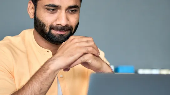 Un hombre con barba mira la pantalla de una laptop con satisfacción
